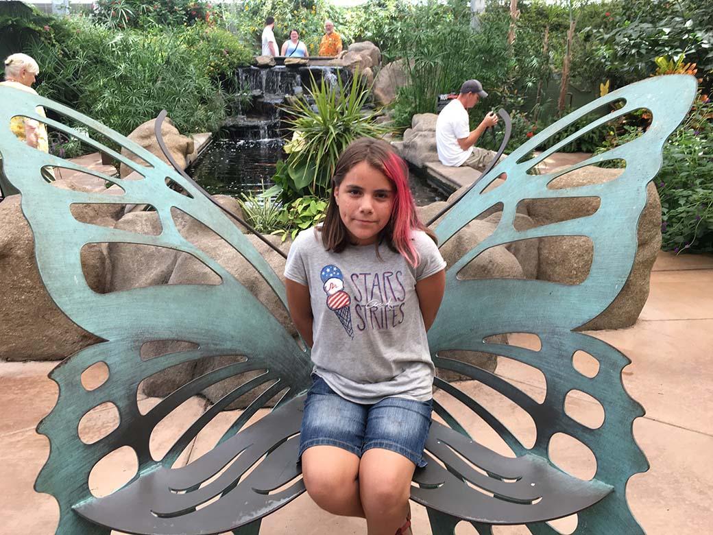 This is a photo of Mia, a New Pathways for Youth mentee. She is photographed inside a butterfly sculpture at an outdoor garden.
