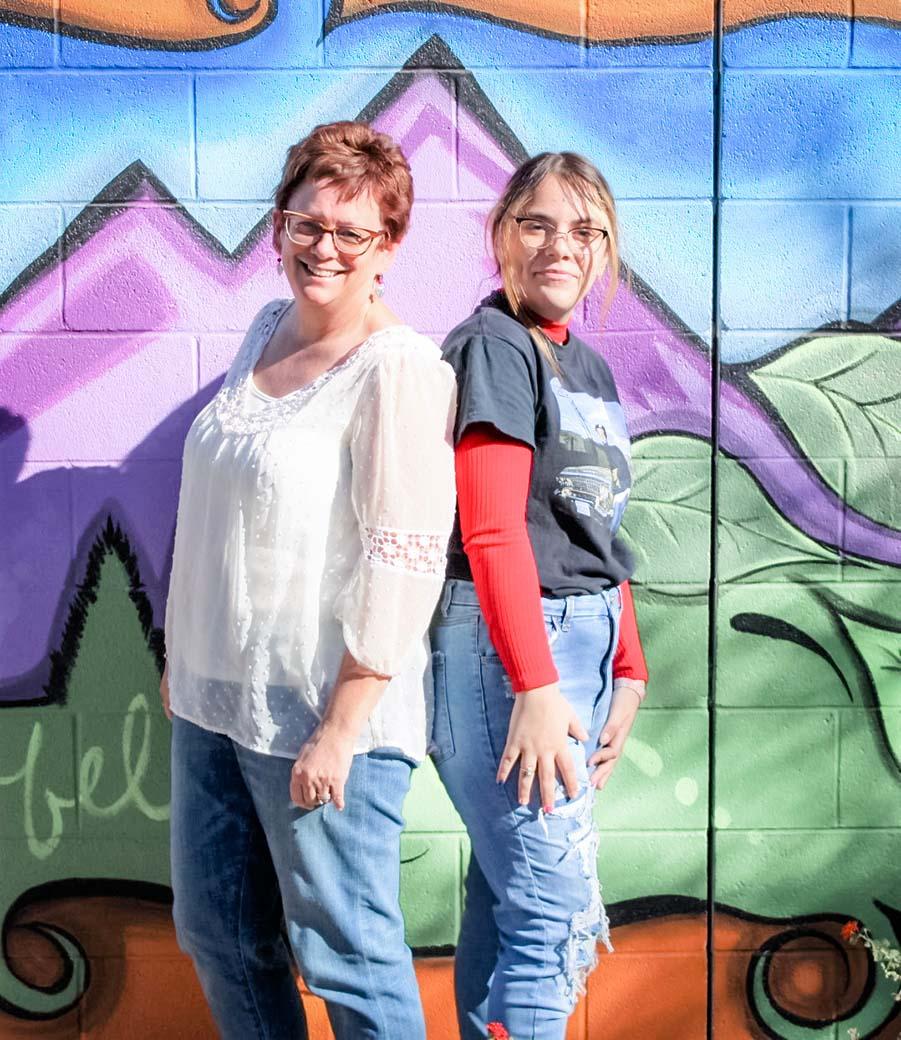 This is a photo of Mia and Jeri. They have a successful mentor-mentee relationship with New Pathways for Youth. They are photographed in front of a wall mural.